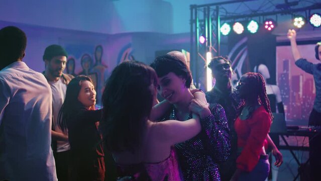 Young partners dancing in pairs at party, moving on dance floor and partying at nightclub. Couples having fun with romantic slow music at disco party, colorful lights club. Handheld shot.