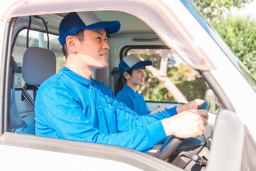 トラックに乗って運転をする業者の男女（引越し・配達・軽貨物ドライバー・宅配・配達員・宅急便）
