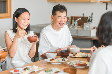 家のダイニングで家族団欒して食事する孫と老夫婦・親子・三世代家族（帰省・里帰り）
