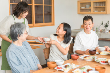 家のダイニングで家族団欒して食事する子供と夫婦・親子・三世代家族（二世帯住宅）
