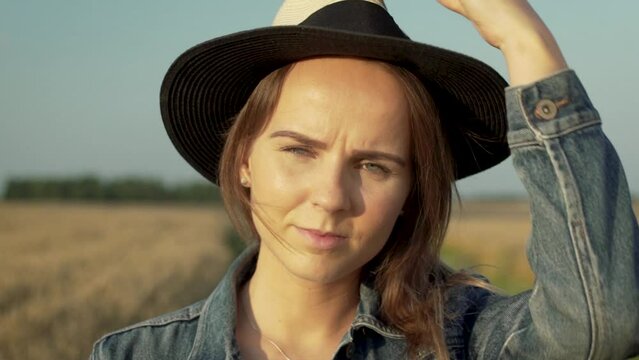 Attractive girl standing in front of camera and putting her stylish summer hat on. Lady is wearing denim jacket witch gives nice travel and summer style to the footage.