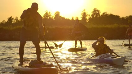 friends paddle boarding and kayaking in golden sunset slomo summer fun
