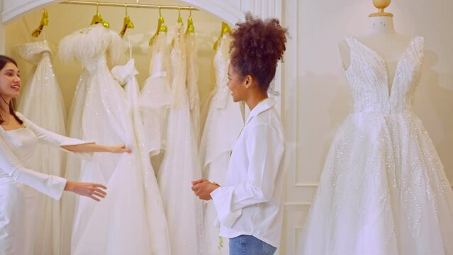 Beautiful bride trying the wedding dress with helper female in studio.