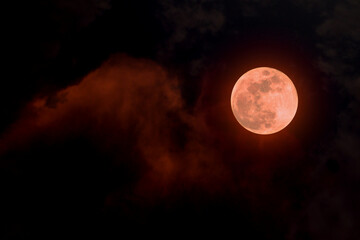 Image of a cloudy sky at night with a red full moon.