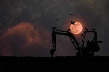 Silhouette of an excavator parked on the ground with a flock of crows at night with a full red moon.
