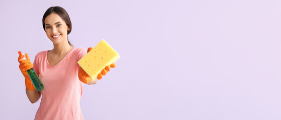 Young woman with rubber gloves, cleaning sponge and detergent on lilac background with space for text