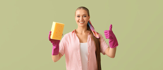 Happy young woman with rubber gloves and cleaning sponge showing thumb-up gesture on green...