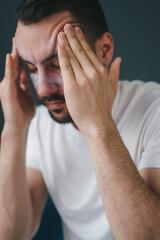 Close-up portrait of a man, sitting at home on the sofa in the living room with eyes closed, suffering from a headache, massaging his temples. Closeup portrait.