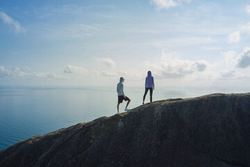 Two people standing on top of the mountain, looking at the ocean and the sky beneath, admire the...