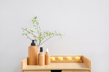 Bath accessories with candles and tree branches on table near light wall