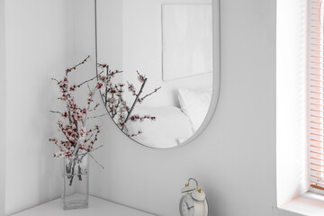 Vase with blooming tree branches on commode in light bedroom