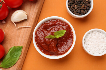 Bowl of tomato sauce and board with ingredients on orange background