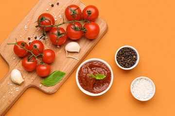 Bowl of tomato sauce and board with ingredients on orange background