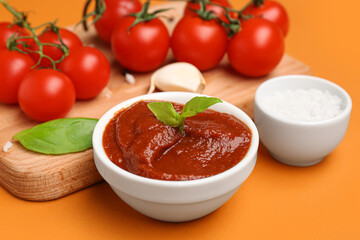 Bowl of tomato sauce and board with ingredients on orange background, closeup