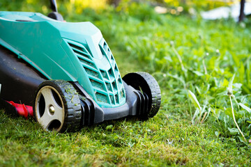 electric lawn mower in the garden near the house on a partially mowed lawn, copy space