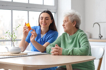 Young caregiver and senior woman taking pills in kitchen