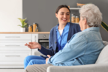 Fototapeta premium Young caregiver with senior woman sitting on sofa at home