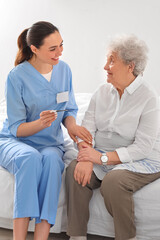 Obraz premium Young caregiver with thermometer and senior woman in bedroom
