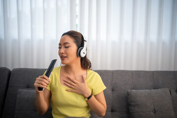 Woman wearing headphones and listening to music and singing happy at home on vacation.