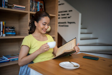 woman sitting at home reading a book and drinking coffee on vacation