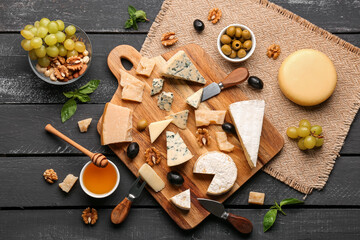 Board with different types of tasty cheese, nuts, honey and grapes on dark wooden background