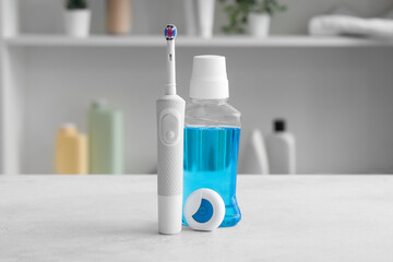 Dental floss with electrical toothbrush and mouthwash on white table in room