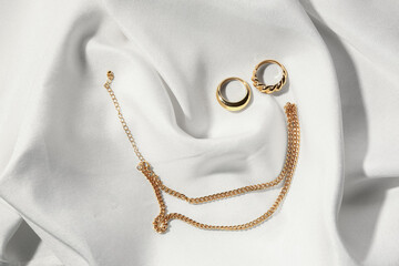 Beautiful chain necklace and rings on white fabric background