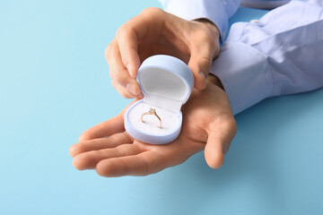 Man holding box with engagement ring on blue background, closeup