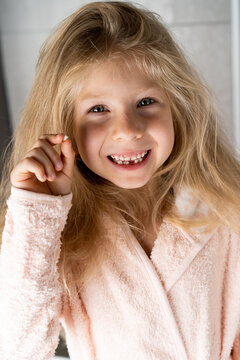 a little blonde girl shows a fallen baby tooth and smiles, close-up, vertical photo