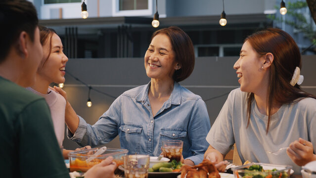 Middle aged mom smile joy look at young grown up kid child with love care good warm time. Asia people woman adult older mum parent sitting at home night dinner outdoor house party happy life moment.