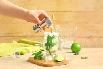 Female bartender making tasty mojito cocktail on table near wooden wall