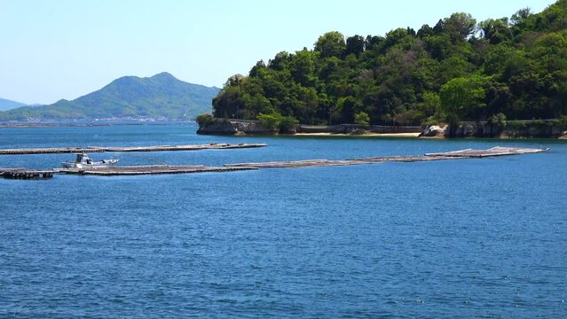 瀬戸内海、広島湾に浮かぶ牡蠣養殖筏と島の風景を船から移動撮影  4K  2023年4月23日 広島湾の宇品島・似島付近にて撮影。