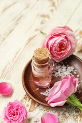 Fototapeta na wymiar Bottle of cosmetic oil with rose extract and flowers on light wooden table