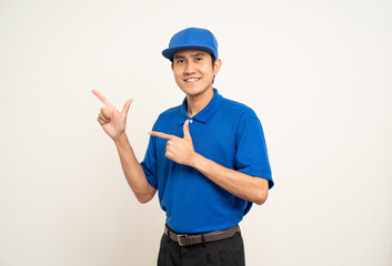 Happy delivery asian man in blue uniform standing on isolated white background. Smiling male service worker pointing the finger to blank space. Delivery courier and shipping service.