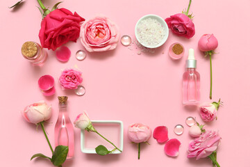 Frame made with bottles of cosmetic oil, rose flowers and salt on pink background