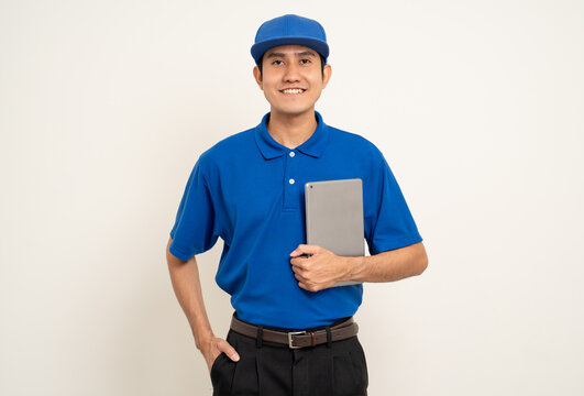 Asian man in blue uniform standing holding digital tablet computer on isolated white background. Male service worker with cell phone. Delivery courier shipping service