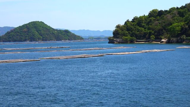 瀬戸内海、広島湾に浮かぶ牡蠣養殖筏と島の風景を船から移動撮影  4K  2023年4月23日 広島湾の宇品島・似島付近にて撮影。