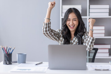 Excited Asian young woman using phone and laptop sitting on a desk office in the day at office
