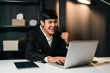 Young asian businessman working with laptop computer in the dark office at night. Attractive...