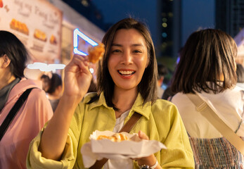 Asian woman enjoy eating fries street food at night market. Traveler Asian blogger women Happy tourists Beautiful female with Traditional thailand bangkok food.