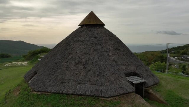 Rise and pullback over historic Jomon thatched roof hut on Awaji Island