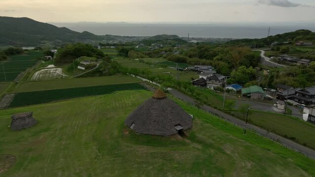 Approaching historic Jomon thatched roof hut on hill over small village on coast