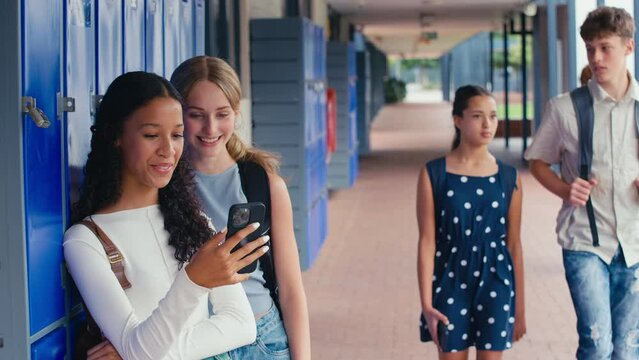 Two female high school or secondary students looking at social media or internet on mobile phone by lockers - shot in slow motion