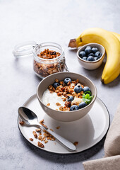 Muesli with vegetarian yogurt, banana and blueberries in a bowl on a gray texture background. Healthy and dietary homemade granola for breakfast.