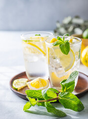Lemonade drink with fresh lemons, lime, mint and ice. Refreshing citrus mojito cocktail on a light background. Summer cold drinks concept.