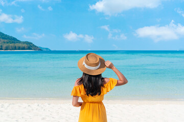 Rear view of happy traveler Asian woman on yellow dress relax on the tropical sandy beach. Summer, holiday concept. Copy space, closeup