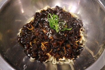 Jajangmyeon on a big alumunium bowl before stirring. jjajangmyeon is a Korean-style Chinese noodle dish topped with a thick sauce made of chunjang, diced pork, and vegetables.
