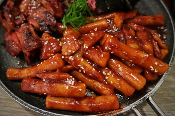 Close-up of tteok-bokki on a hot pan, stir-fried rice cake is a popular Korean dish. Spicy sauce with added gochujang. Sprinkle with roasted sesame seeds.