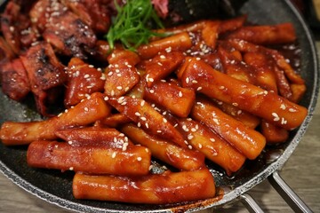 Close-up of tteok-bokki on a hot pan, stir-fried rice cake is a popular Korean dish. Spicy sauce with added gochujang. Sprinkle with roasted sesame seeds.