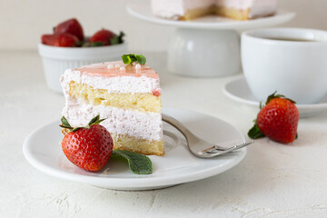 A slice of strawberry-cream cake lies on a white saucer. Ripe strawberries on the table. A cup of...